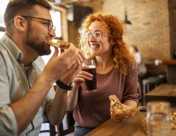 two people eating pizza and drinking beer at a restaurant 